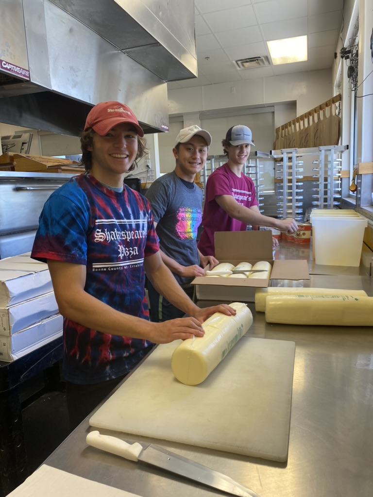 Three people preparing cheese smiling at the camera.