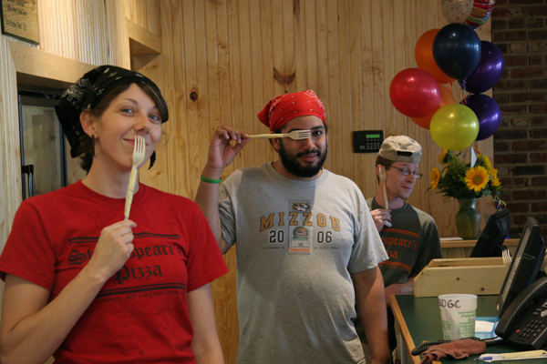 One person putting a fork on their mouth and one person putting a fork over their eye.